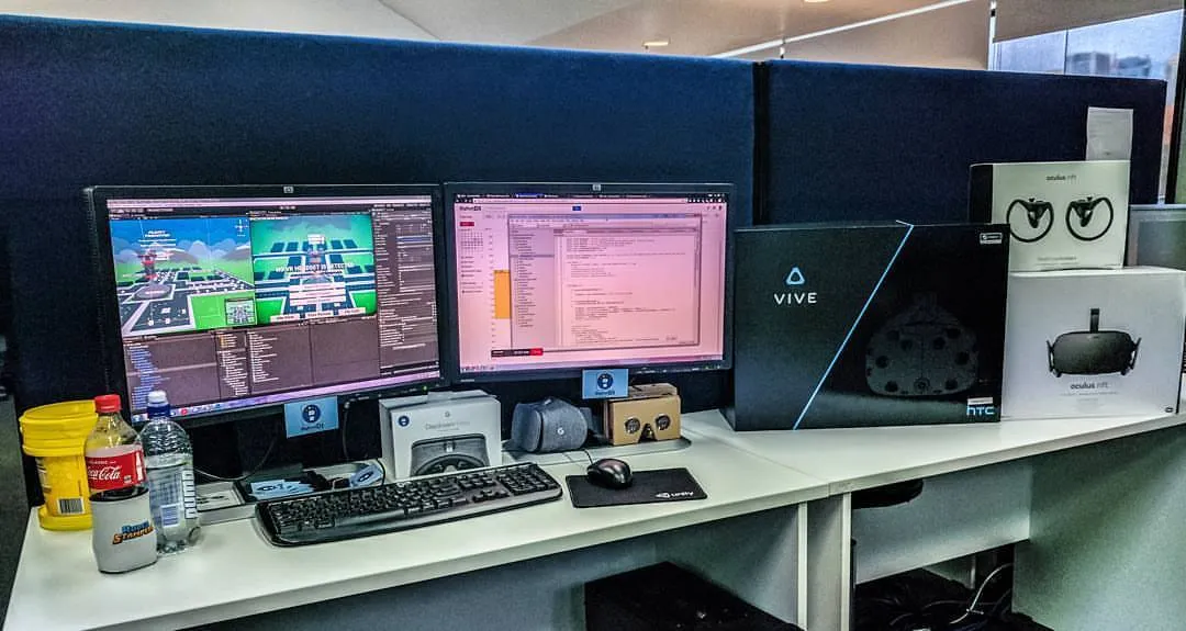 A photo of a software developer’s workspace. It includes a computer, keyboard, mouse, two monitors, two Google Daydream VR headsets, one Google Cardboard VR headset, one HTC Vive VR headset, and one Oculus Rift VR headset. VR development takes a lot of hardware!